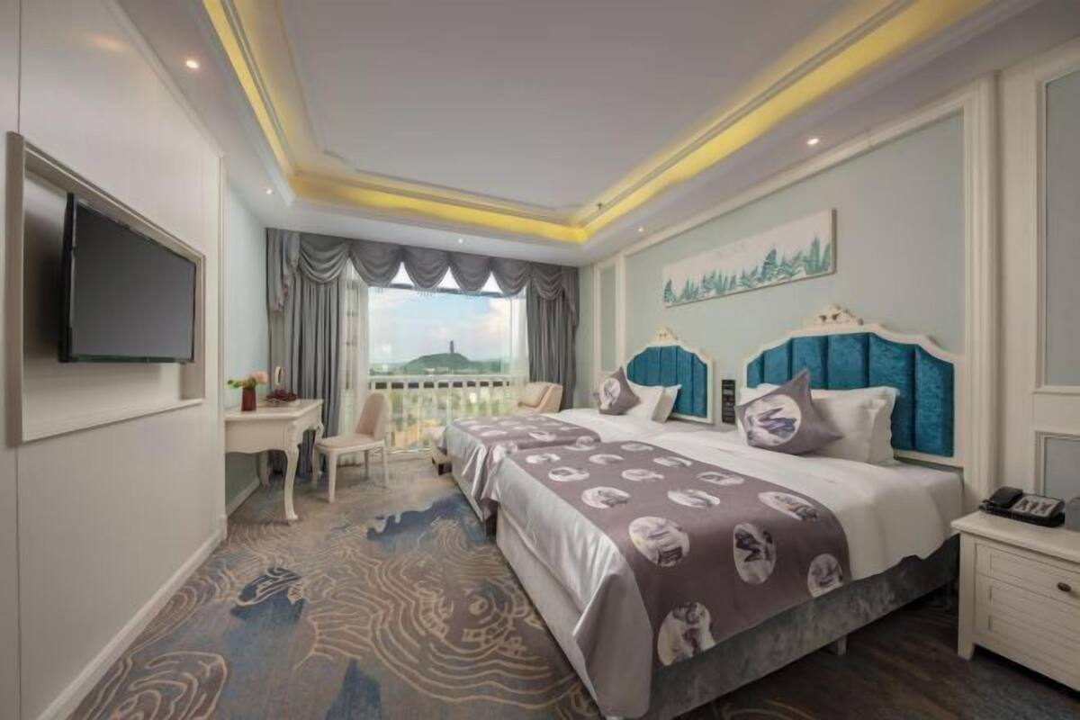 Ein Hotelzimmer mit einem großen Bett, einem an der Wand befestigten Fernseher, einem Schreibtisch und Blick ins Freie.