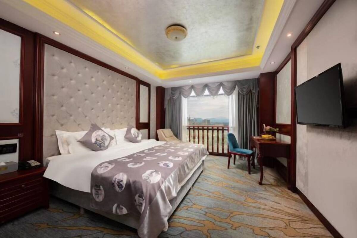 Ein Hotelzimmer mit einem großen Bett, einem Fernseher, einem Schreibtisch mit Stuhl und einem Balkon mit Blick.