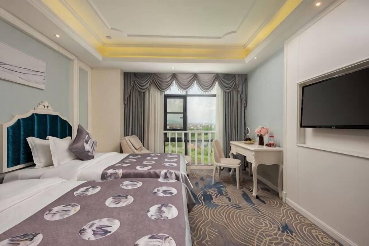 Ein Hotelzimmer mit zwei Betten, einem Schreibtisch, einem Stuhl, einem Fernseher und einem Balkon mit Aussicht.