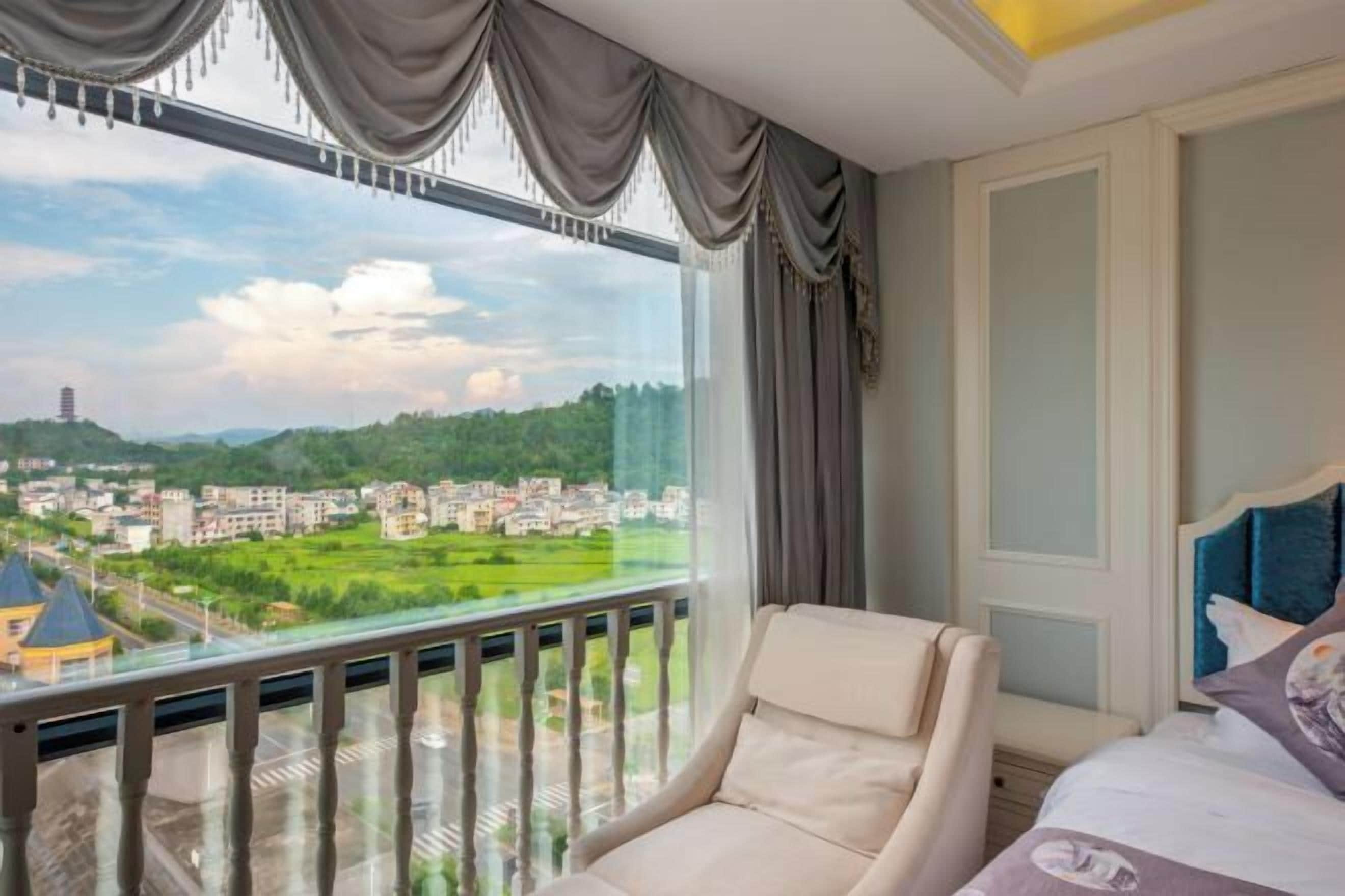 A hotel room with a large window offering a view of a cityscape and greenery.