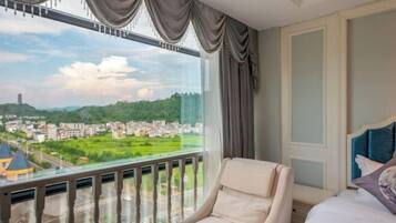 A hotel room with a large window offering a view of a cityscape and greenery.