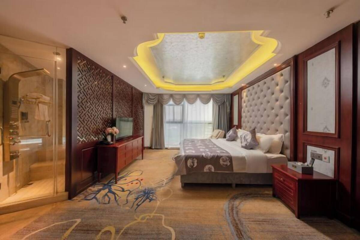 Ein modernes Hotelzimmer mit einem großen Bett, einer Duschkabine aus Glas, einer dekorativen Wandverkleidung und einem einzigartigen Deckenstil.