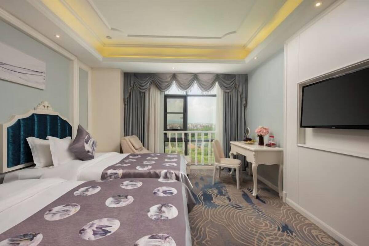 Ein Hotelzimmer mit zwei Betten, einem Schreibtisch, einem Stuhl, einem Fernseher und einem Balkon mit Blick.