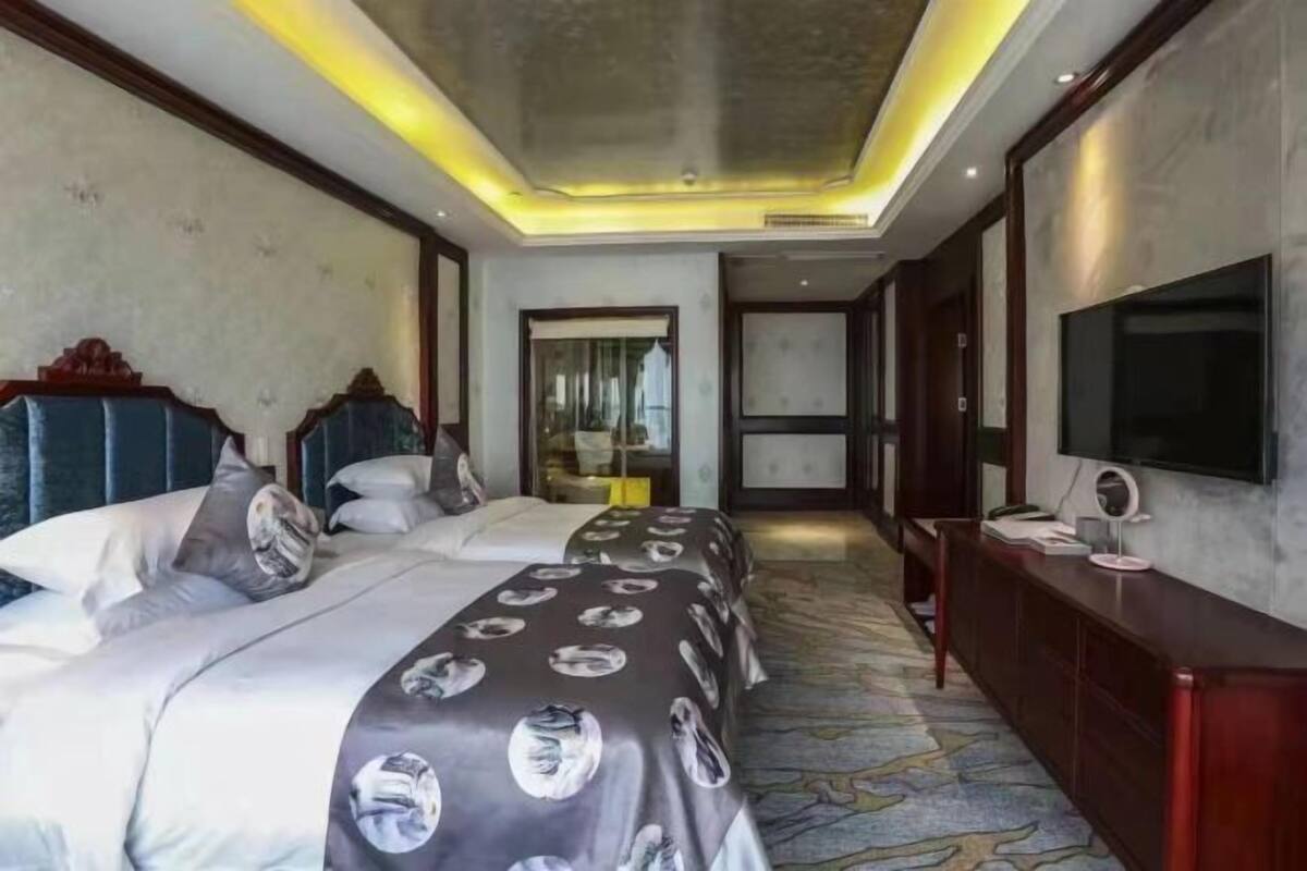 Ein Hotelzimmer mit zwei Betten, einem großen Spiegel, einem Fernseher und einem Teppichboden.