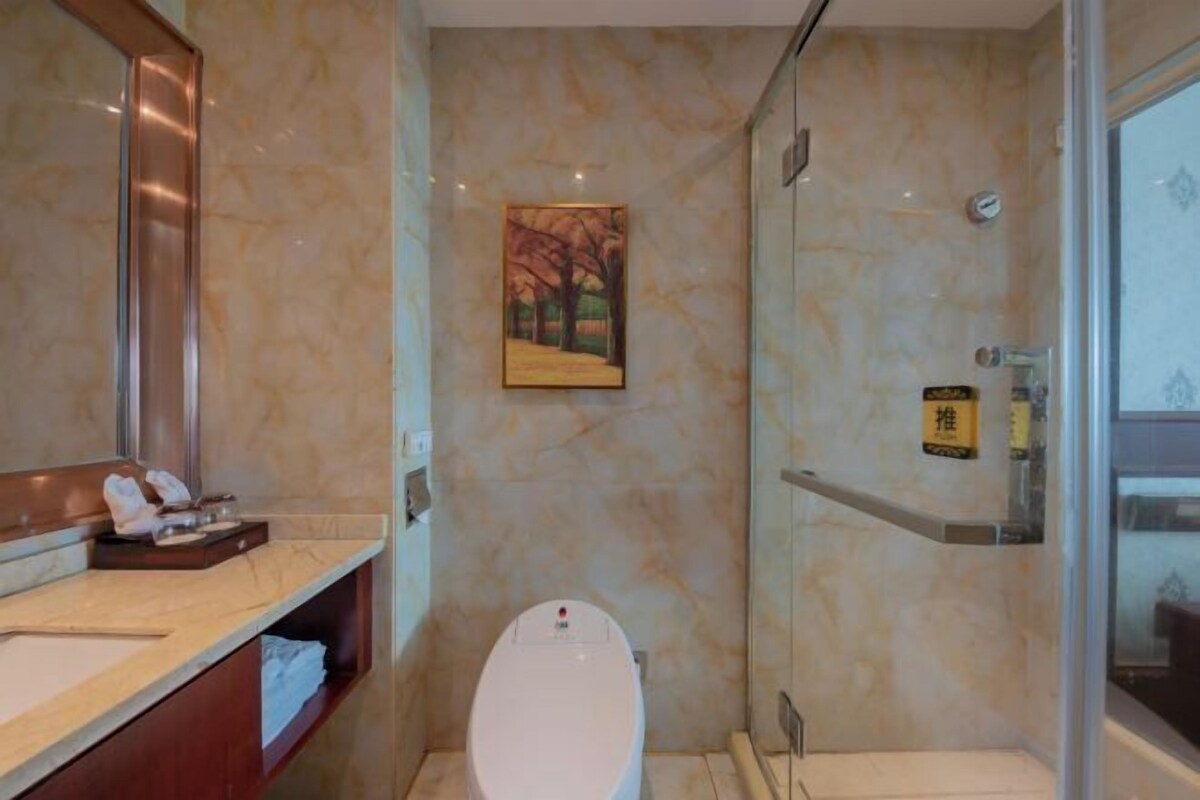 Une salle de bain avec un mur en marbre, des toilettes, un espace douche et un lavabo avec un miroir.