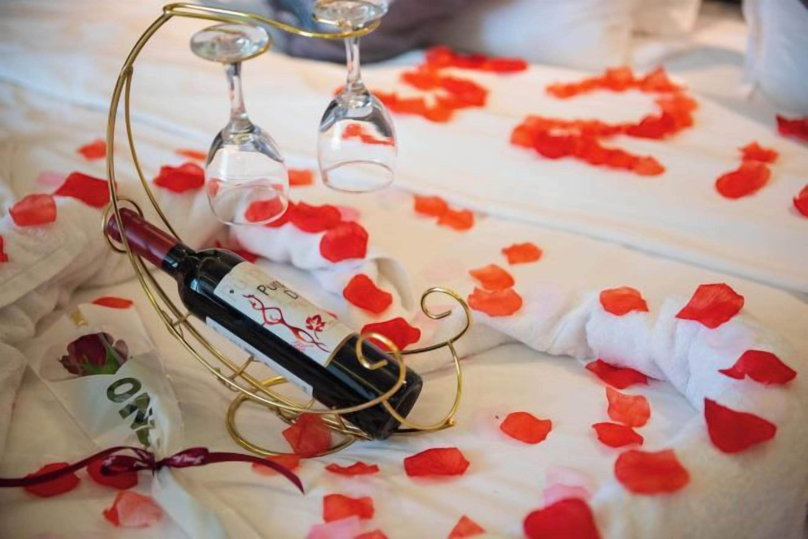 A bottle of wine on a table with rose petals and a wine glass.