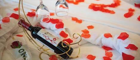 A bottle of wine on a table with rose petals and a wine glass.