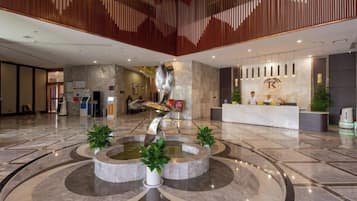 A spacious lobby with a central fountain, reception desk, and modern decor.