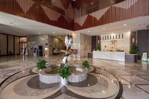 Een ruime lobby met een fontein in het midden, een receptiebalie en een modern interieur.