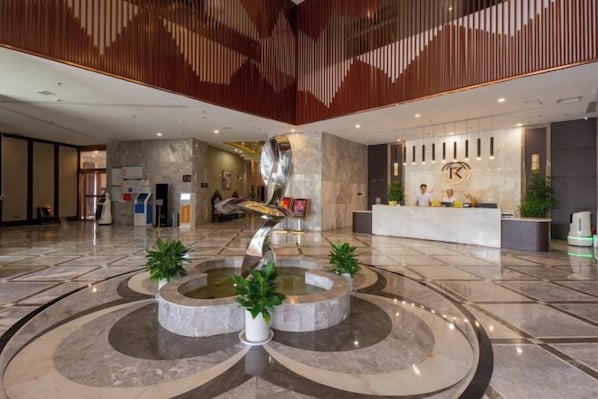 A spacious lobby with a central fountain, reception desk, and modern decor.