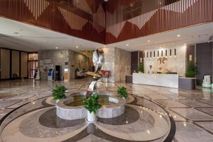 Un vestíbulo amplio con una fuente central, mostrador de recepción y decoración moderna.