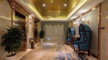 A hotel lobby with a marble floor, a chandelier, and two blue armchairs.