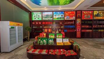 A hotel lobby with a central display of food products, a refrigerator, and shelves with various items.