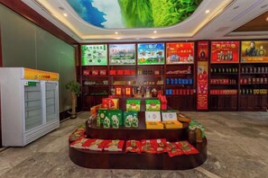 Un hall d'hôtel avec un présentoir central où sont exposés des produits alimentaires, un réfrigérateur et des étagères remplies de divers articles.