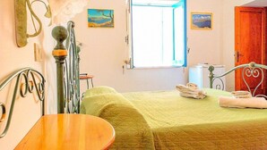 Una habitació amb llit, taula, làmpada i dos quadres a la paret.