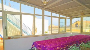 Una stanza con un lungo tavolo ricoperto da una tovaglia viola, sedie verdi e ampie finestre che danno vista su un edificio con una scala.