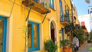 Un edificio giallo con finestre a cornice blu, un balcone e piante in vaso.
