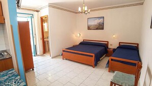 Une chambre à coucher avec deux lits en bois, un lustre, un tableau accroché au mur et une salle de bain visible à travers une porte ouverte.