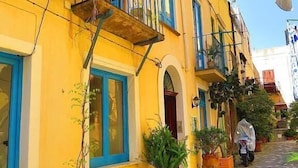 Un bâtiment jaune avec des fenêtres à encadrement bleu, un balcon et des plantes en pot.