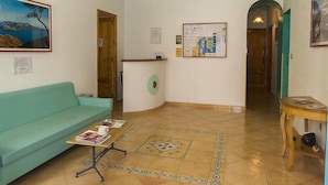 Une pièce avec un canapé de couleur turquoise, une table en bois sur laquelle sont posés des magazines, un tableau d’affichage et un lustre.