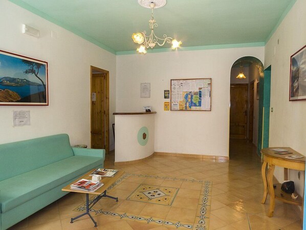 Une pièce avec un canapé de couleur turquoise, une table en bois sur laquelle sont posés des magazines, un tableau d’affichage et un lustre.