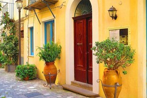 Une rue étroite bordée d’immeubles jaunes, avec une porte rouge et des plantes en pot.