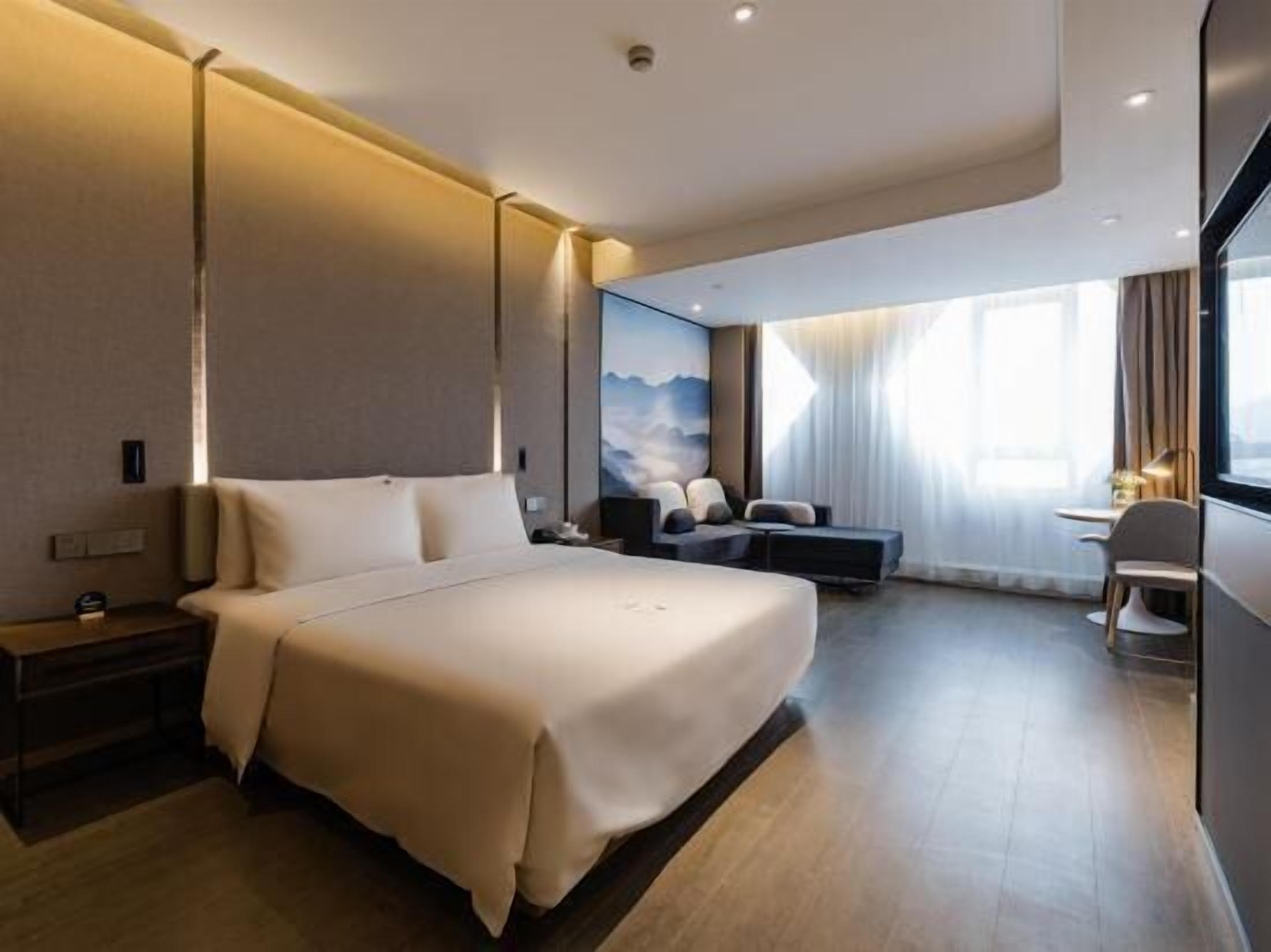 A modern hotel room with a large bed, a desk, and a seating area.
