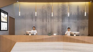 A reception desk with two staff members, a large wall mural, and a digital display. - Atour Hotel (Ningbo)