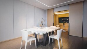 A modern dining area with a marble table and white chairs, a small side table, and a decorative piece on the wall. - Atour Hotel (Ningbo)