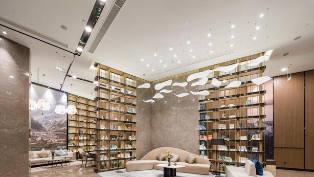 A modern interior with a large sectional sofa, a coffee table, and a bookshelf filled with books. - Atour Hotel (Ningbo)