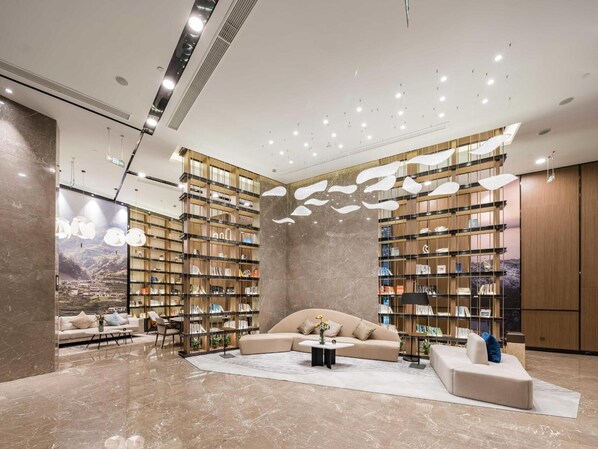 A modern interior with a large sectional sofa, a coffee table, and a bookshelf filled with books. - Atour Hotel (Ningbo)