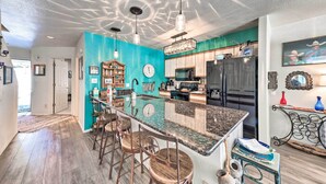 A kitchen with a central island, bar stools, a clock, and a refrigerator. - Bright Cloudcroft Condo w/ Game Room + Deck! (Cloudcroft)