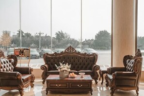 Eine Lobby mit einer großen Säule, einem braunen Sofa, zwei Sesseln und einem Couchtisch mit Vase und Kerzen.