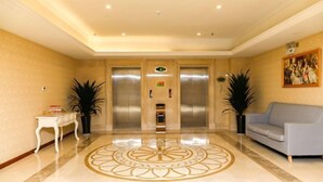 Una hall d'albergo con pavimento in marmo lucido, due ascensori, una reception e un divano.