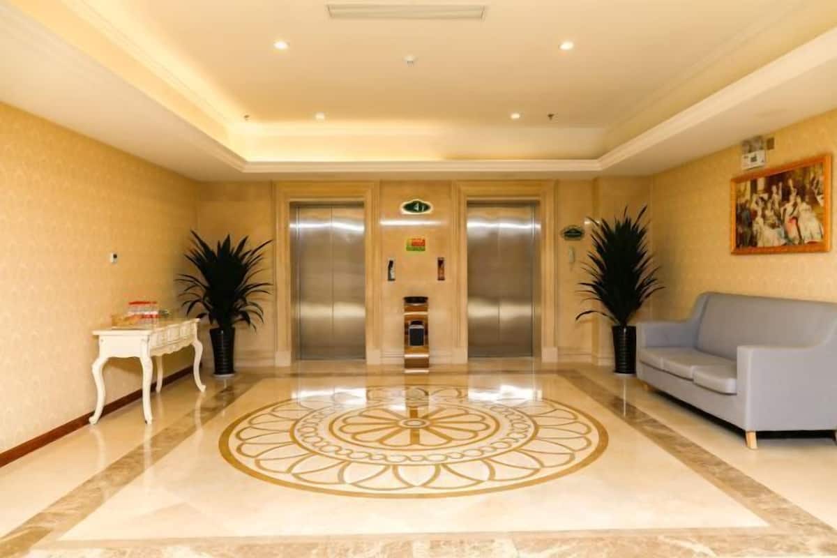 A hotel lobby with a polished marble floor, two elevators, a reception desk, and a sofa.