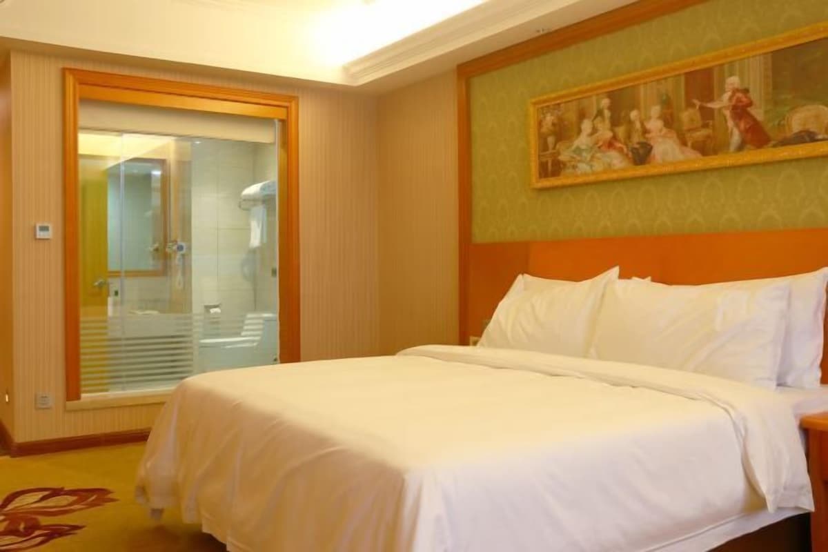 Una habitación de hotel con una cama grande, una ducha y un cuadro en la pared.