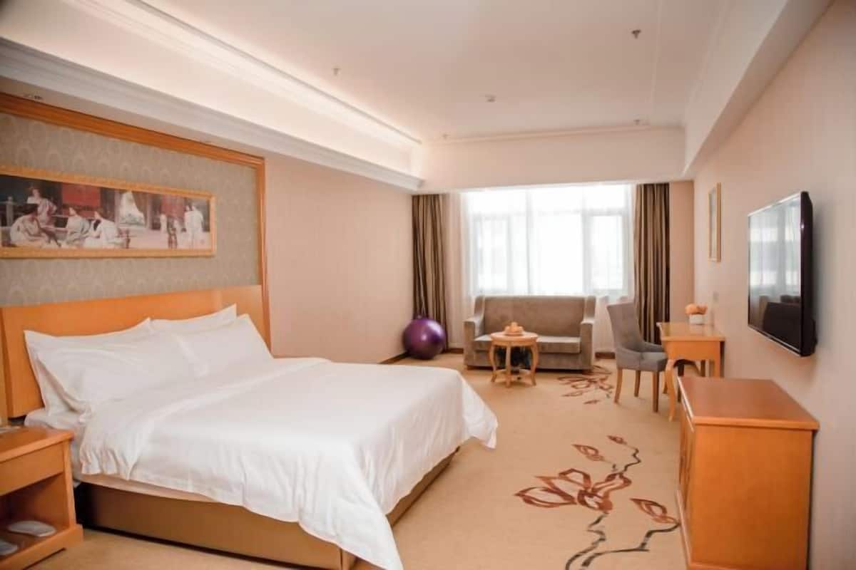 A hotel room with a large bed, a sofa, a TV, and a painting on the wall.