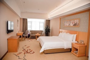 Una habitación de hotel con una cama grande, un escritorio, una silla, un televisor y una ventana con cortinas.