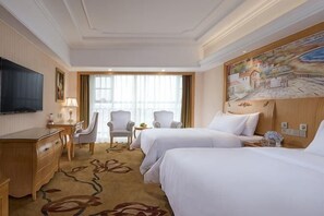 A hotel room with two beds, a desk, a chair, a TV, and a painting on the wall.