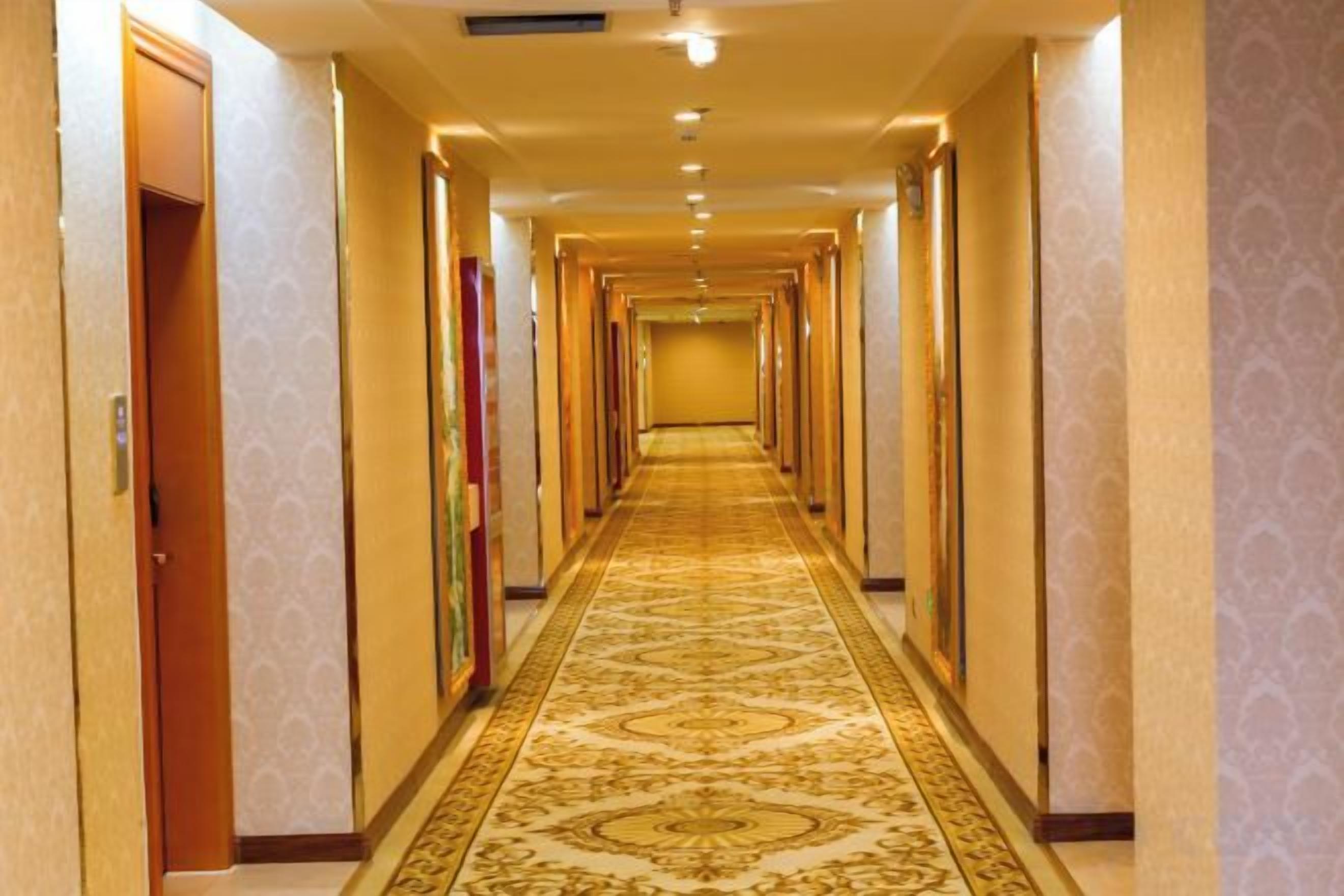 A long, narrow hotel corridor with carpeted floors and doors on both sides.