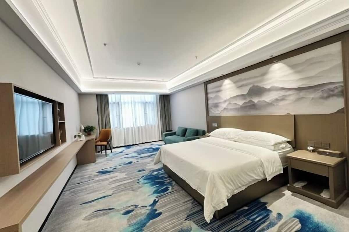 A hotel room with a bed, a TV, a desk, a chair, and a painting on the wall.