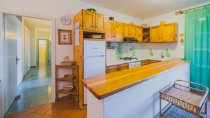 A compact kitchen with wooden cabinets, a white refrigerator, and a green curtain.