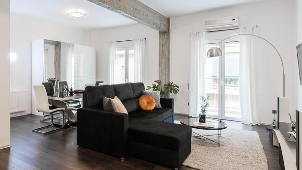A modern living room with a black sofa, a glass coffee table, and a large mirror.
