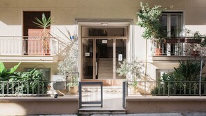 A building entrance with a door, a small balcony with a railing, and potted plants.