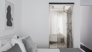 A modern hotel room with a bed, a large framed artwork, and a glass-enclosed shower area.