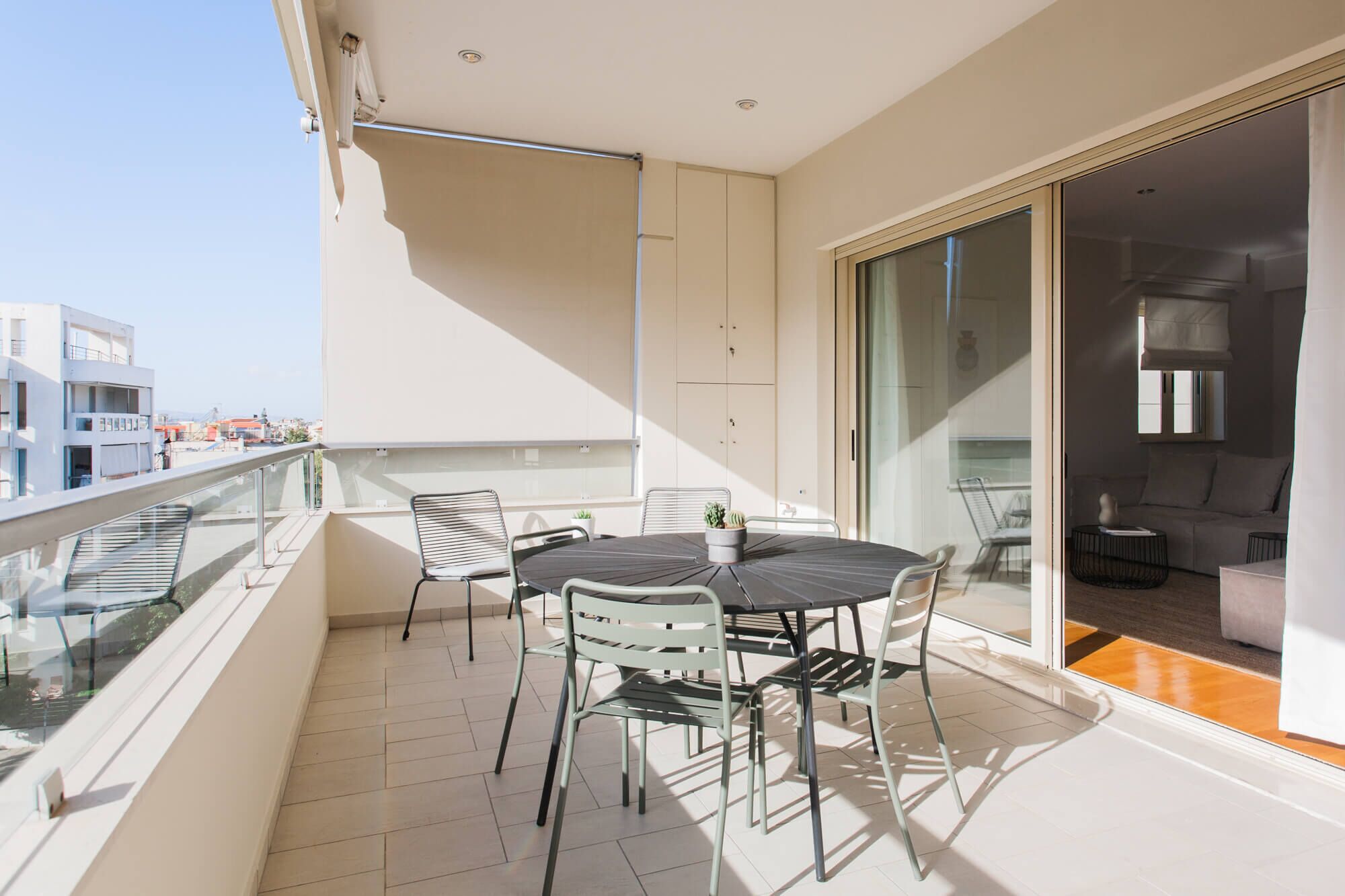 Un balcon doté d’une balustrade en verre, une table ronde avec des chaises et une porte-fenêtre coulissante donnant sur un espace de vie.