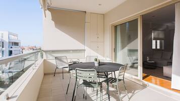 Un balcon doté d’une balustrade en verre, une table ronde avec des chaises et une porte-fenêtre coulissante donnant sur un espace de vie.