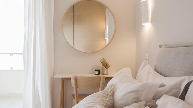Una camera d'albergo con un letto, una scrivania, una sedia, uno specchio rotondo e un portalampada a parete.