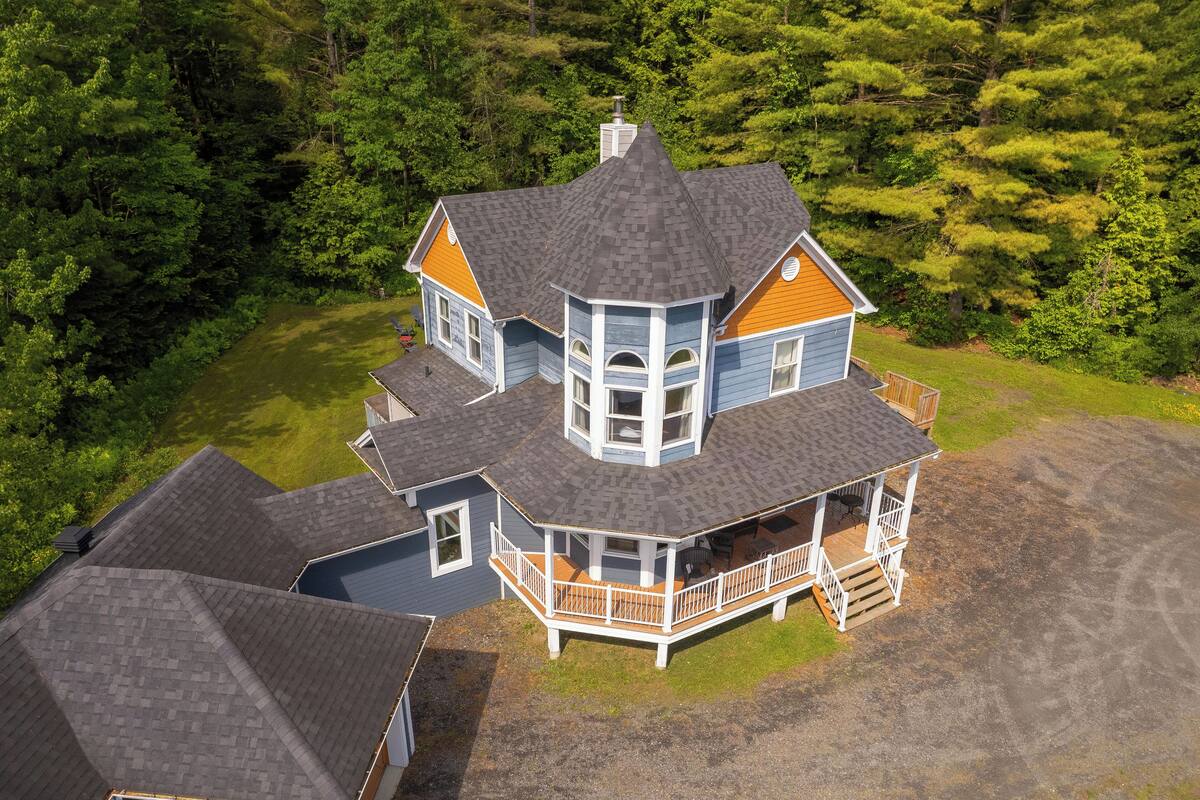 A large, multi-story house with a wrap-around porch and a tower-like structure.