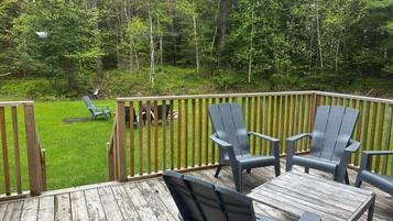 A wooden deck with outdoor furniture, including chairs and a table, overlooking a grassy area with trees.